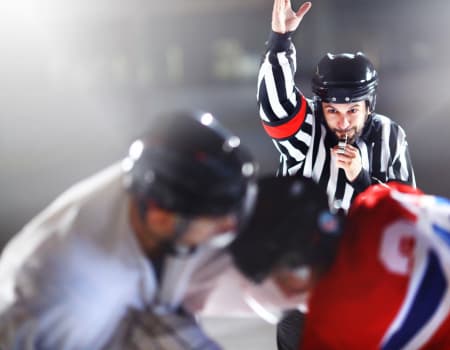 Ice Hockey Referee with hand up at face off of a power play. Two players lean towards the puck drop