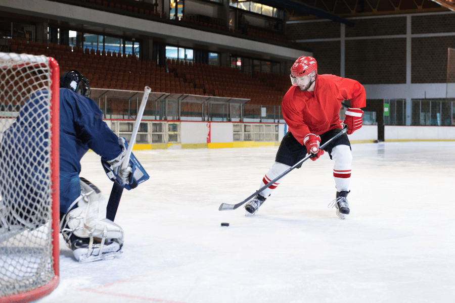 Ice Hockey player in Red determined to meet goals making play on a goalie